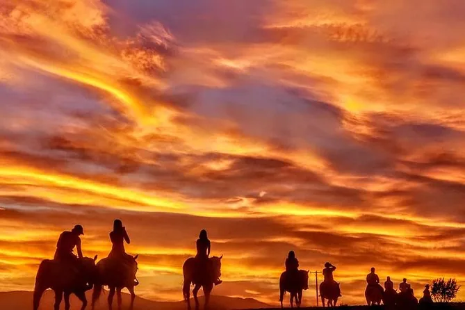 Reiter als Silhouetten vor einem leuchtend orangen Sonnenuntergang in der Wüste